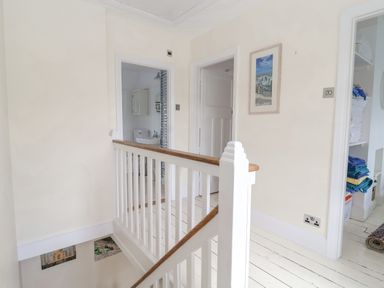 A hallway with white wooden railing leading to doors and a closet with folded towels at Halsey in Walberswick