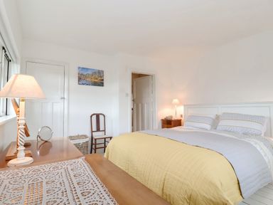 A bedroom with a bed covered with a yellow and gray quilt a wooden chair two lamps and a picture on the wall at Halsey in Walberswick