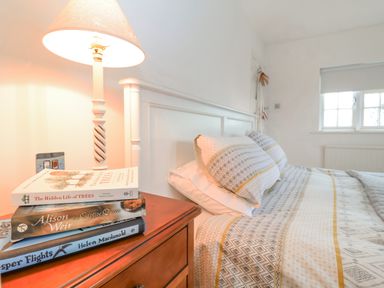 A bedroom with a bed with patterned bedding and pillows next to a wooden nightstand with a lamp and three stacked books at Halsey in Walberswick