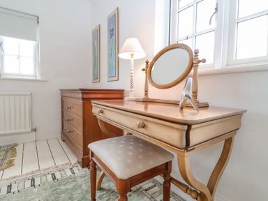 A bedroom corner with a wooden vanity table mirror stool lamp and chest of drawers at Halsey in Walberswick