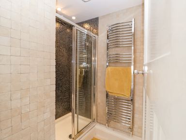 A bathroom shower area with glass sliding doors a chrome towel rack holding a yellow towel and tiled walls at Halsey in Walberswick