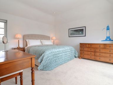 A bedroom with a bed with a blue comforter two lamps wooden dresser and wooden table with mirror at Halsey in Walberswick