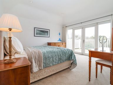 A bedroom with a bed side table lamp a dresser a vanity table with a mirror and glass doors leading to a balcony at Halsey in Walberswick