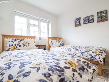 A bedroom with two single wooden beds with floral bedding a nightstand between the beds and three pictures on the wall at Halsey in Walberswick