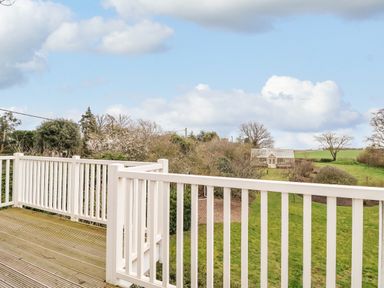 A wooden deck with white railing overlooking a garden with a greenhouse and trees at Halsey in Walberswick