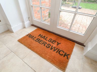 An orange doormat with text on tiled floor in front of glass doors at Halsey Walberswick