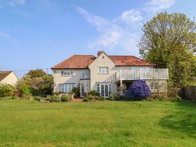 A two story house with a red roof a large green lawn and various shrubs and trees at Halsey in Walberswick