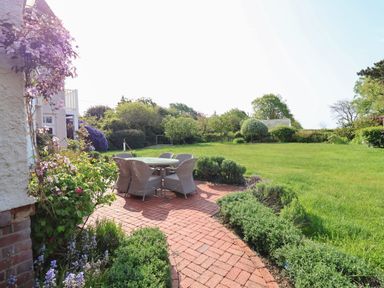 A garden with a round table and six chairs on a brick patio surrounded by plants at Halsey in Walberswick