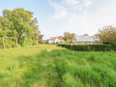 A grassy garden with a swing set on the left and a greenhouse on the right with a house in the background at Halsey in Walberswick