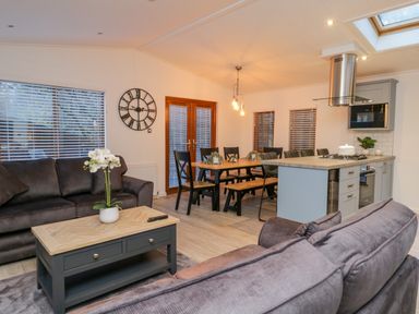 A living area with sofas and a coffee table next to a dining table and a kitchen at 25 Thirlmere in Troutbeck Bridge