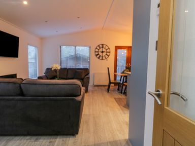 A living area with two dark sofas a wall mounted television a clock and a dining table with chairs at 25 Thirlmere in Troutbeck Bridge