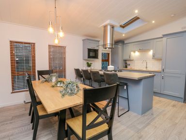 A kitchen with blue cabinets a wooden dining table with black chairs and pendant lights at 25 Thirlmere in Troutbeck Bridge