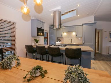 A kitchen with a wooden table with plants bar stools and grey cabinets at 25 Thirlmere in Troutbeck Bridge
