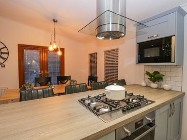 A kitchen with a gas stove and white pot on the counter near a dining table with black chairs and wooden doors at 25 Thirlmere in Troutbeck Bridge