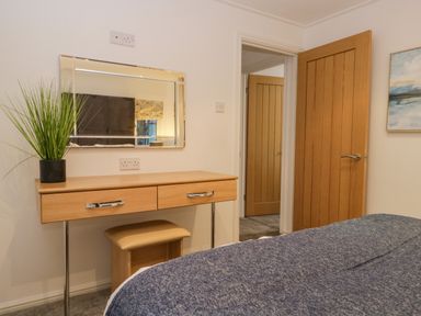 A bedroom with a wooden dressing table with mirror and plant a partially visible bed and two wooden doors at 25 Thirlmere in Troutbeck Bridge