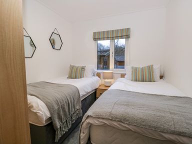 A bedroom with two single beds a bedside table with lamp two hexagonal mirrors and a window at 25 Thirlmere in Troutbeck Bridge