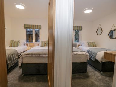 Two adjacent bedrooms each with two single beds bedside table and window at 25 Thirlmere in Troutbeck Bridge
