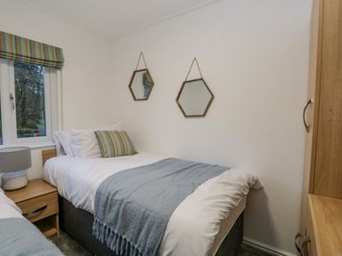 A bedroom with two single beds a nightstand with a lamp a window two hexagonal mirrors and a wardrobe at 25 Thirlmere in Troutbeck Bridge