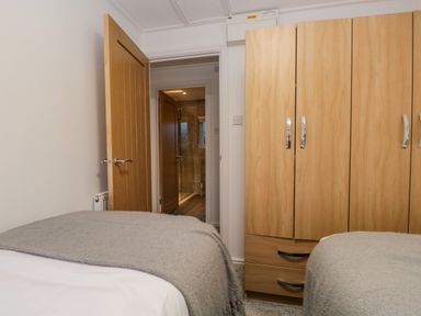 A bedroom with two beds and a wooden wardrobe next to an open door showing a bathroom at 25 Thirlmere in Troutbeck Bridge