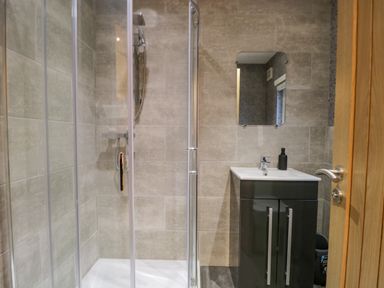 A bathroom with a glass shower enclosure a sink with cabinet a mirror and a wooden door at 25 Thirlmere in Troutbeck Bridge