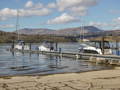 A dock with boats moored on a lake with hills and trees in the background at 25 Thirlmere in Troutbeck Bridge