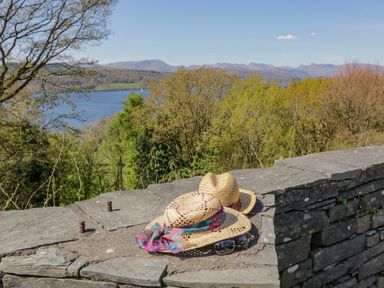 Two straw hats and sunglasses on a stone wall with trees and a lake in the background at 25 Thirlmere in Troutbeck Bridge