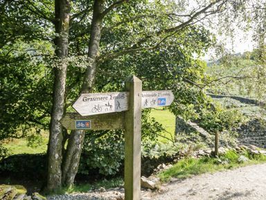 A wooden signpost by a tree showing directions to Grasmere and Ambleside on a countryside path at 25 Thirlmere in Troutbeck Bridge