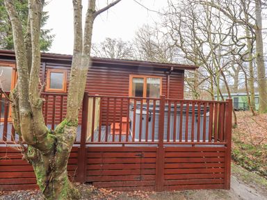 A wooden cabin with a fenced porch and trees around at 25 Thirlmere in Troutbeck Bridge