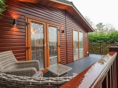 An outdoor wooden deck with wicker chairs and a table next to a cabin at 25 Thirlmere in Troutbeck Bridge