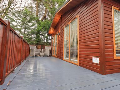 An outdoor deck with two wicker chairs and a small table next to a wooden cabin at 25 Thirlmere in Troutbeck Bridge