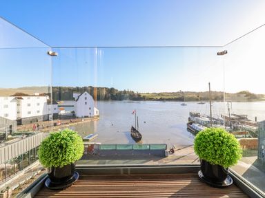 A balcony with two potted plants overlooking a river with boats and buildings at The Penthouse in Woodbridge
