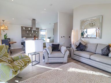 A living room with grey sofas and a green armchair next to a kitchen area at The Penthouse in Woodbridge