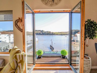 A living area with an open glass door leading to a balcony overlooking a river with a boat at The Penthouse in Woodbridge