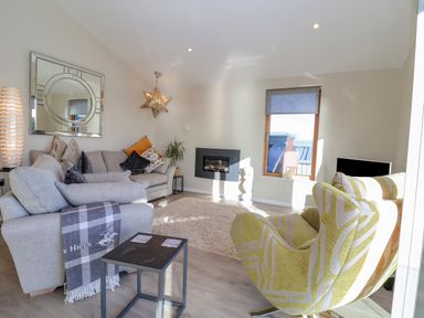 A living room with sofas a window and a wall-mounted fireplace at The Penthouse in Woodbridge