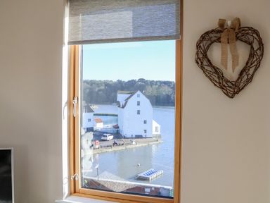 A window with a view of white buildings by water and trees with a heart-shaped decoration on the wall at The Penthouse in Woodbridge