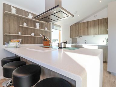 A kitchen with a white countertop bar and black stools wooden cabinets and shelves with white teapots at The Penthouse in Woodbridge
