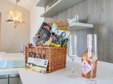 A kitchen counter with a wicker basket filled with snacks and a bottle of organic prosecco with two empty glasses at The Penthouse in Woodbridge