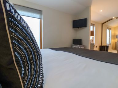 A bedroom with a decorative pillow on the bed a chair with a cushion a wall-mounted TV and large mirror at The Penthouse in Woodbridge