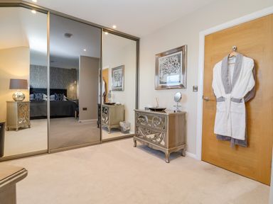 A bedroom with mirrored wardrobe doors a chest of drawers a framed picture and robes hanging on a door at The Penthouse in Woodbridge
