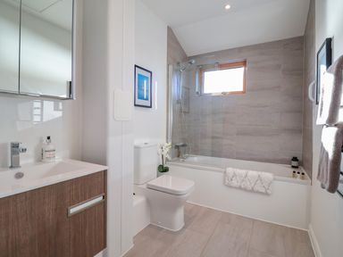 A bathroom with a sink vanity, toilet, bathtub with shower, and a window at The Penthouse in Woodbridge