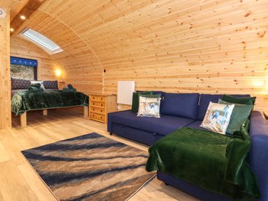 A wooden room with a bed next to a window a wooden dresser a blue sofa with green blankets and pillows and a patterned rug on the floor at The Shearer - Crossgate Luxury Glamping in Hartsop near Glenridding