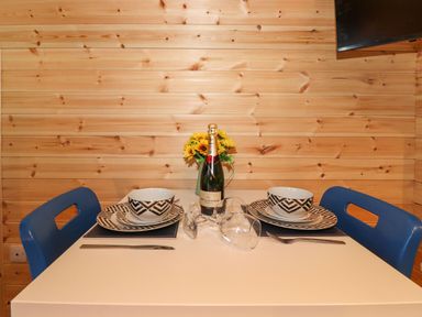 A dining table set with plates bowls wine glasses and a bottle in a wooden room with blue chairs at The Shearer - Crossgate Luxury Glamping Hartsop near Glenridding