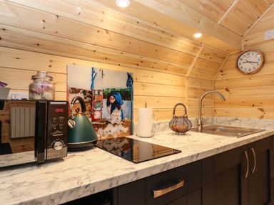A kitchen counter with a microwave, kettle, paper towel holder, wire fruit basket, sink and a wall clock at The Shearer - Crossgate Luxury Glamping in Hartsop near Glenridding