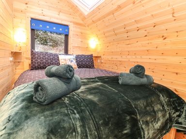 A bed with patterned pillows and rolled towels in a wooden room with a window at The Shearer - Crossgate Luxury Glamping in Hartsop near Glenridding