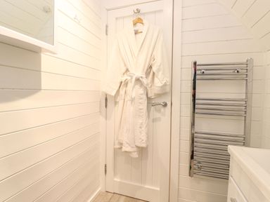 A white bathrobe hanging on a door in a bathroom with a chrome towel radiator at The Shearer - Crossgate Luxury Glamping Hartsop near Glenridding