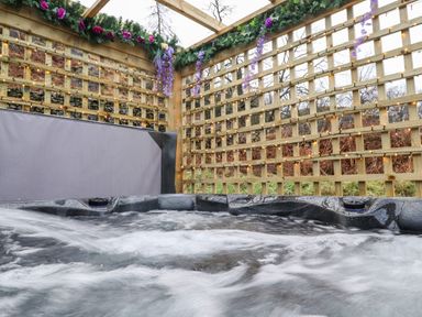 An outdoor hot tub with wooden lattice walls decorated with garlands and string lights at The Shearer - Crossgate Luxury Glamping Hartsop near Glenridding