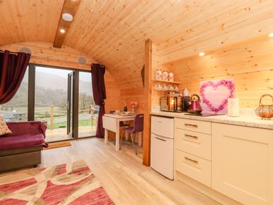 A wooden cabin interior with a small kitchen area a dining table with chairs and a sofa near glass doors at Lovies Place - Crossgate Luxury Glamping in Hartsop near Glenridding