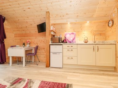 A kitchen area with light wood cabinets a small fridge microwave kettle and a dining table with purple chairs at Lovies Place - Crossgate Luxury Glamping Hartsop near Glenridding