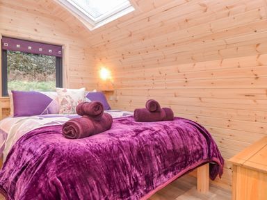 A bedroom with a double bed with purple bedding and rolled towels next to a window and wooden walls at Lovies Place - Crossgate Luxury Glamping in Hartsop near Glenridding