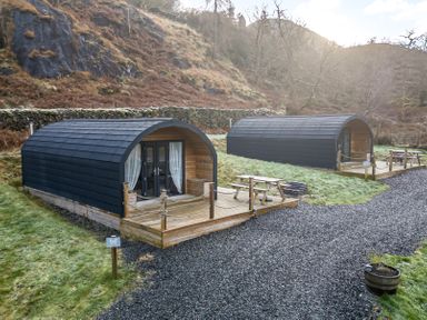 Two wooden camping pods with decks picnic tables and gravel pathways near a hillside at Lovies Place - Crossgate Luxury Glamping Hartsop near Glenridding